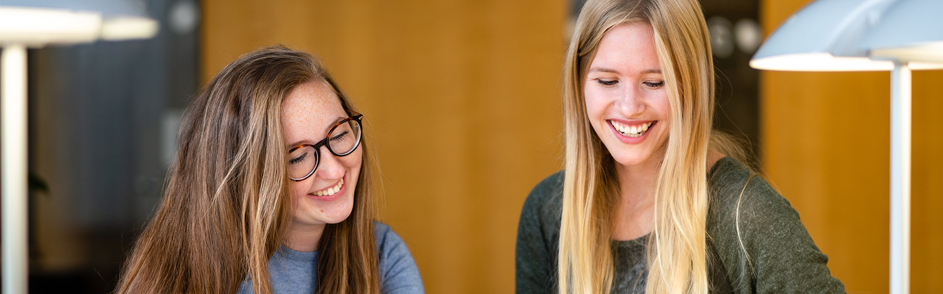 Master of Arts Fachübersetzen Wirtschaft Deutsch/Polnisch - Zwei lachende Studentinnen lesen etwas von einem Zettel ab.