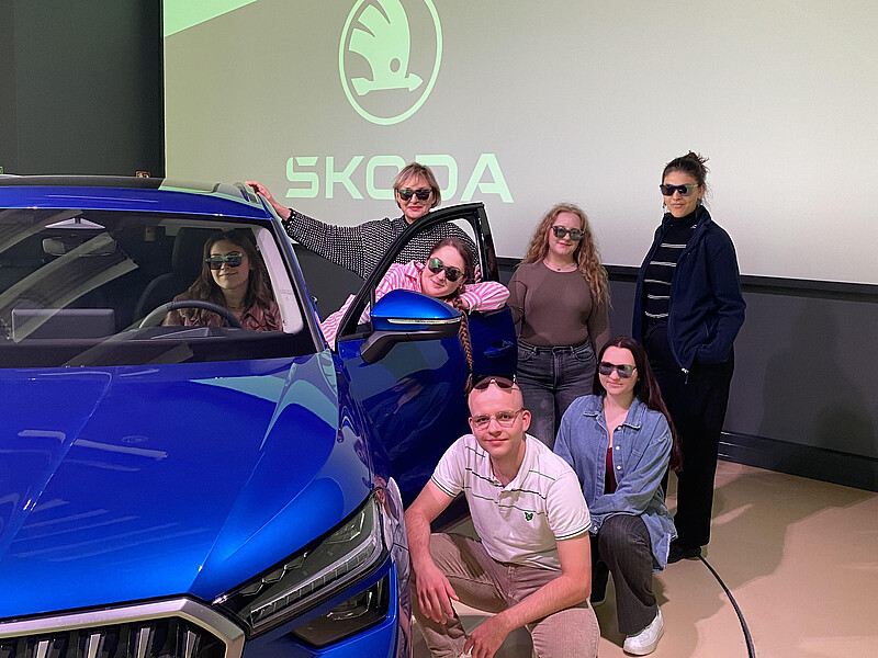 Mehrere Studierende stehen und hocken neben einem blauen Skoda.