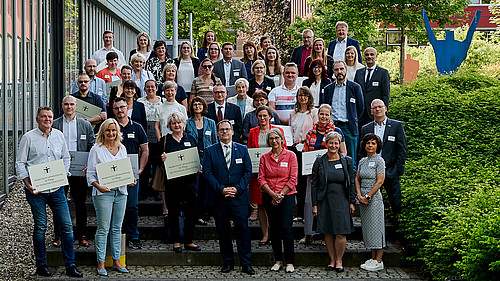 Eine Gruppe aus Hochschulmitgliedern und Kooperationspartnern aus dem Pflegebereich steht neben der Blue-Box am Campus Görlitz.
