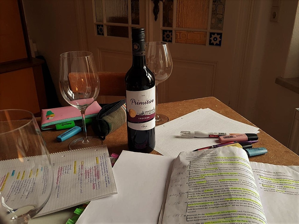 auf einem Tisch, beschriebene Papiere, Stifte, Weingläser und eine Flasche Rotwein