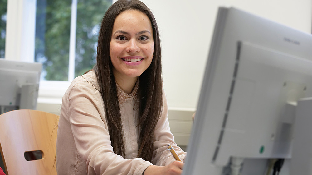 Lächelnde Studentin sitzt vor ihrem PC und recherchiert 