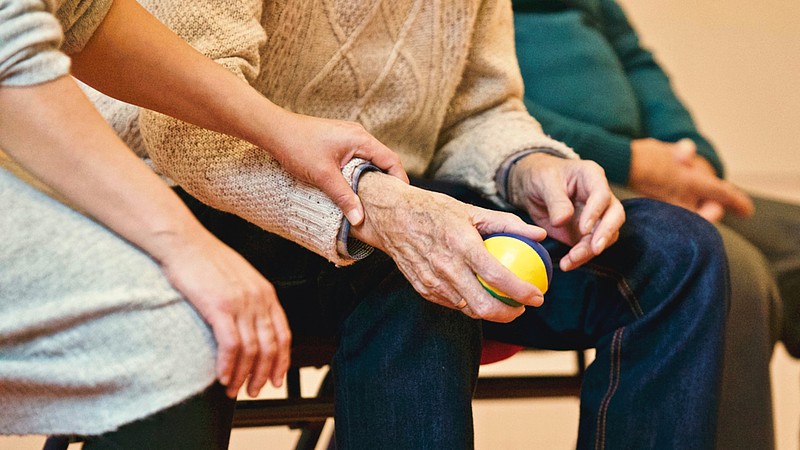 Die Hand einer jüngeren Person drückt auf das Handgelenk einer alten Person, die einen Stressball festhält.